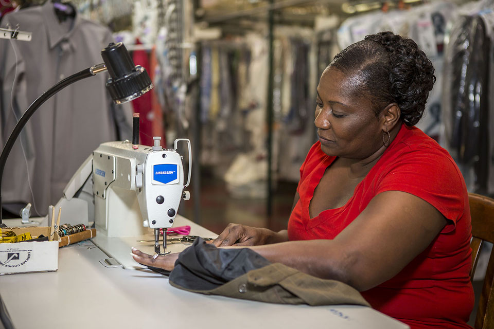 Worker operating the red UNIPRESS HOT machine, pressing a red garment in the in-house workshop