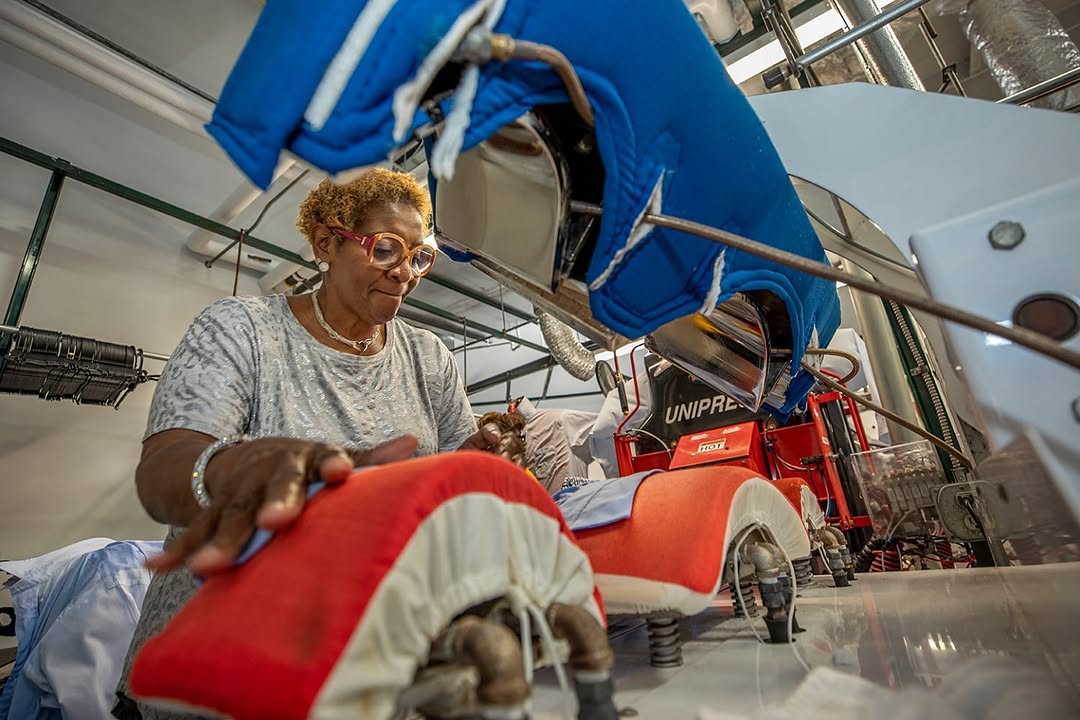 The Complete Cleaners press line in action — a worker operating the red UNIPRESS at the in-house workshop